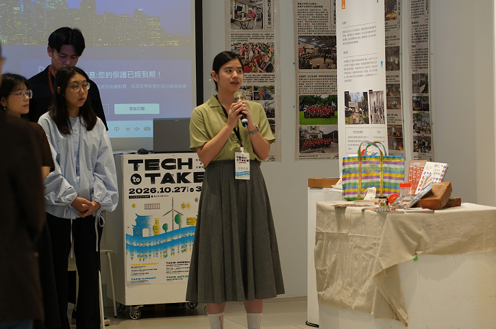 A woman wearing a light green short-sleeved shirt and a gray skirt holds a microphone to give a guided explanation.